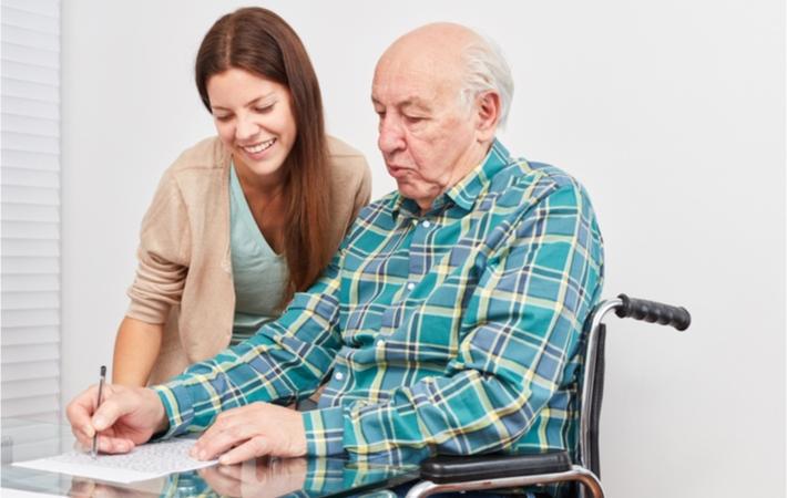 Senior at a senior care facility filling out puzzles to help train his memory with the help of an attendant