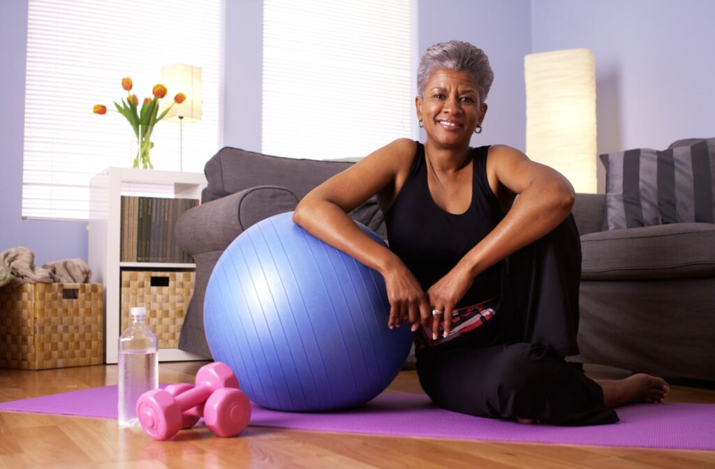 Mature smiling woman sitting on her yoga mat leaning on her exercise ball