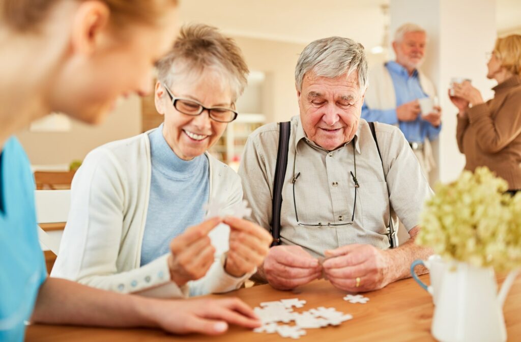 A mature woman and mature man sitting at a table with a young female nurse in a care home working on a puzzle to support their cognitive abilities