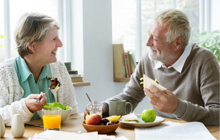 A happy mature couple sitting at a table as they eat a light lunch.