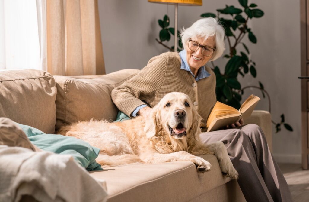 A smiling mature resident is sitting with and petting her dog on the couch.