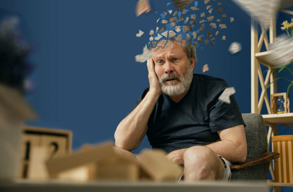 Senior bearded man with alzheimer desease sitting and suffering from headache.