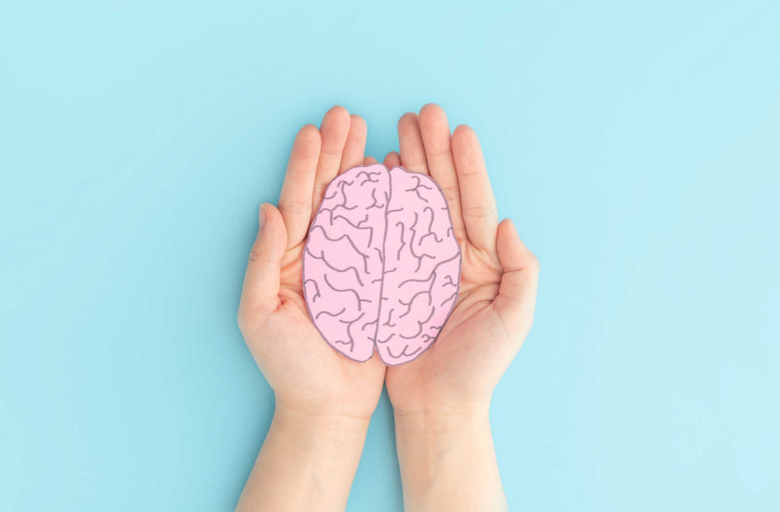 Hands cupped against a blue background holding a paper cutout of a brain.