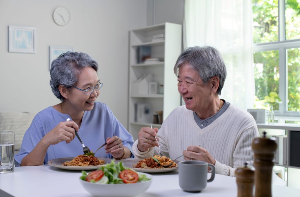 An older adult couple eating a plate of pasta together.