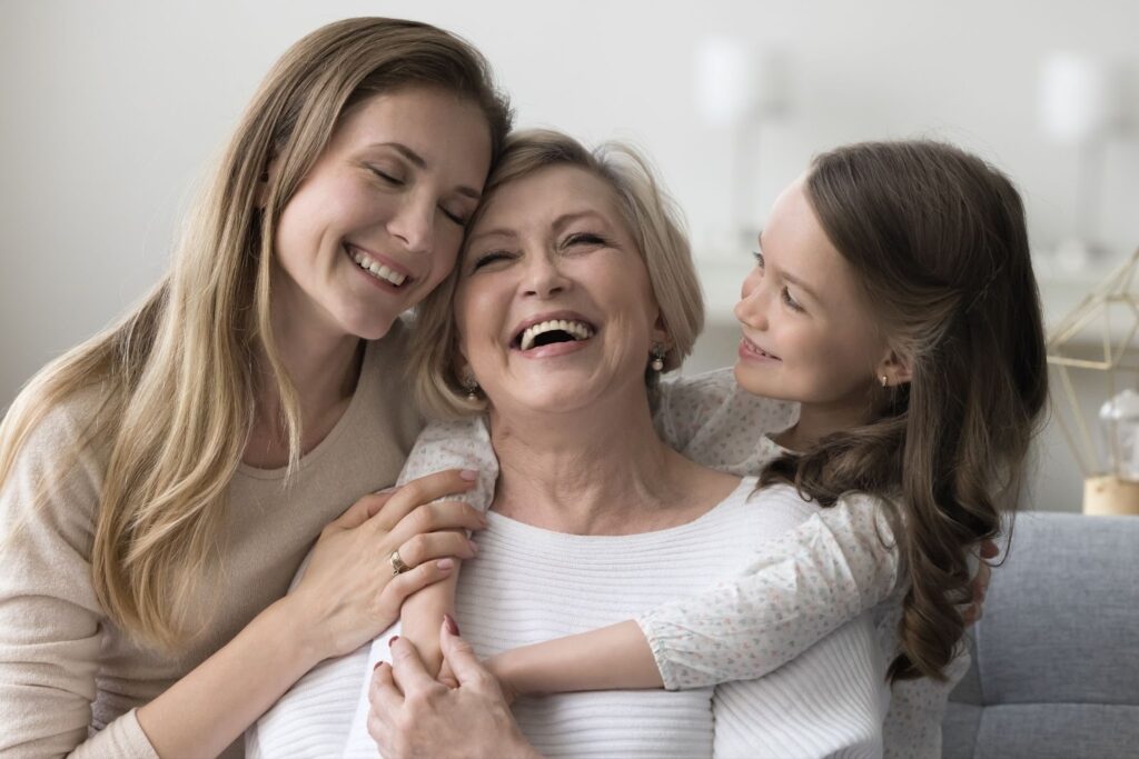 A smiling senior woman hugging her daughter and grandaughter while they visit.