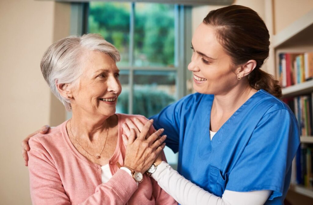 A caregiver putting her arm around a senior woman with dementia. The two are smiling at each other.