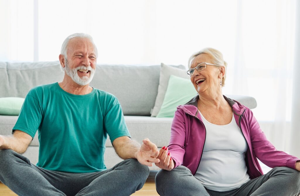 Two seniors sitting on the floor smiling during a yoga session at a seniors care home promoting mindfulness and balance.