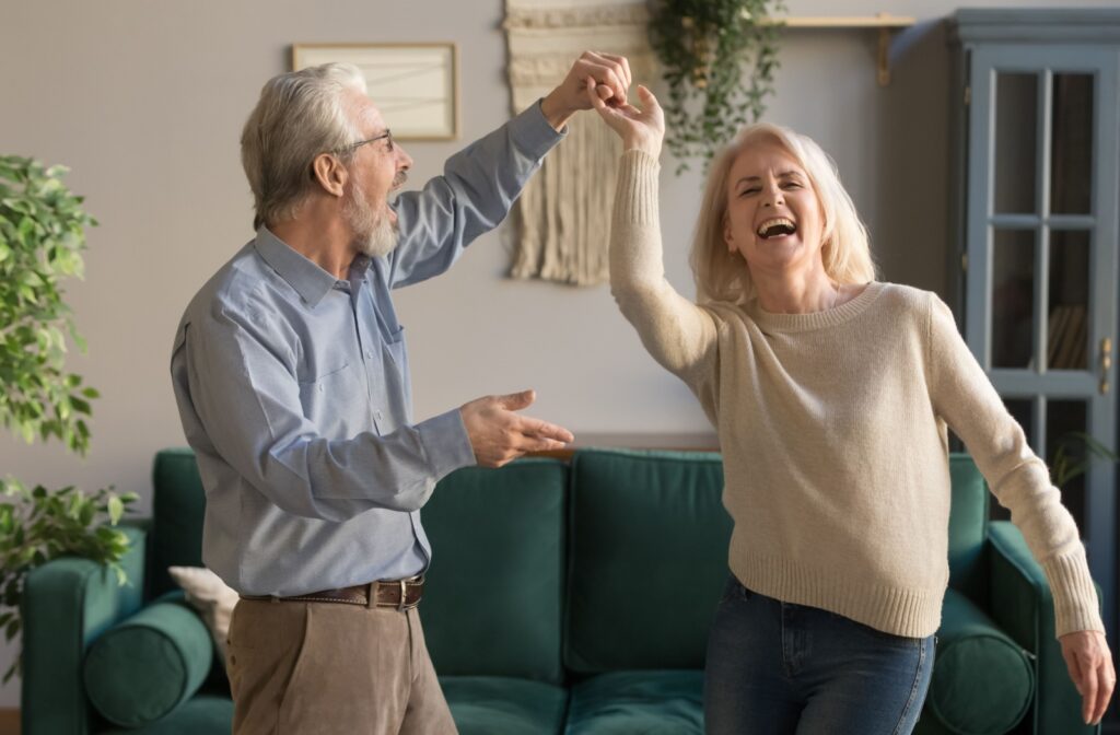 An older retired couple dancing in the living room of their new senior living home.