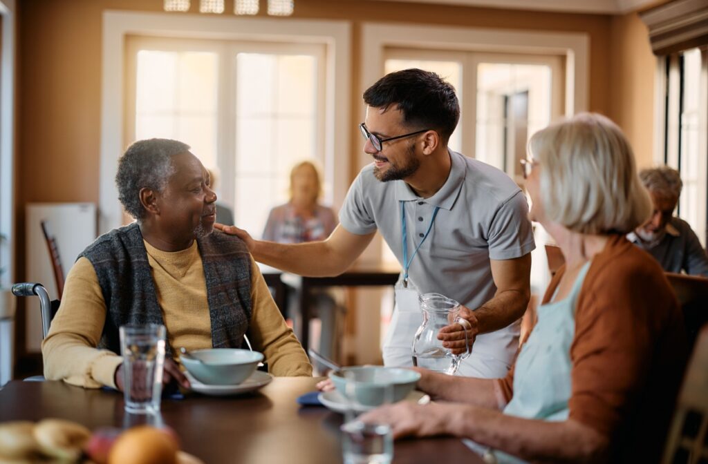 A caregiver checking in on two residents after breakfast time in the common area of a senior living community.