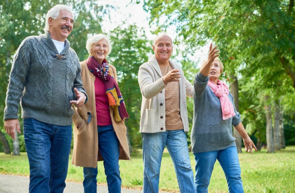 Group of older adults walking on a paved path through a park smiling and talking on a sunny day surrounded by trees