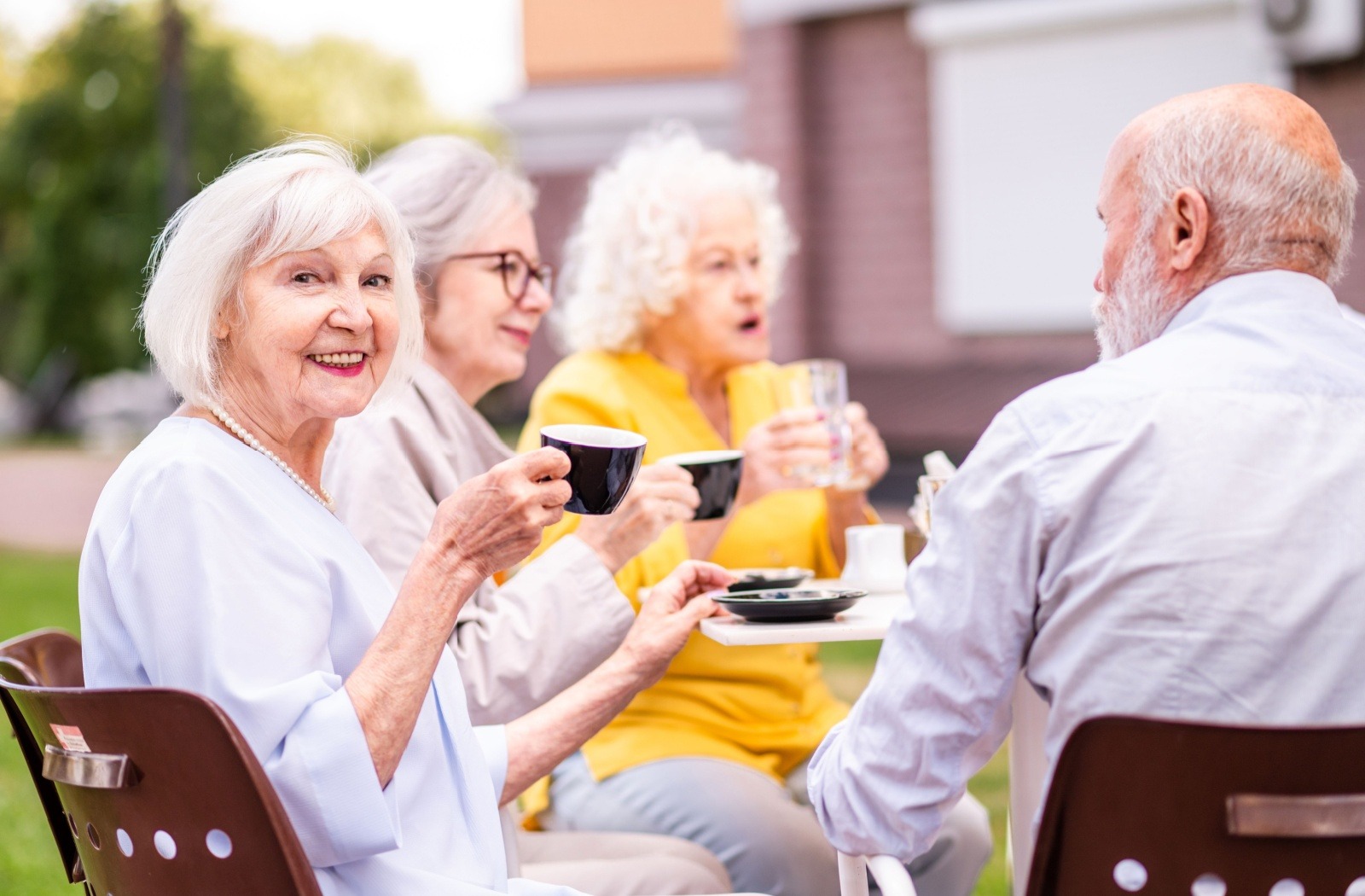 A group of senior friends sit at an outdoor table drinking coffee together.
