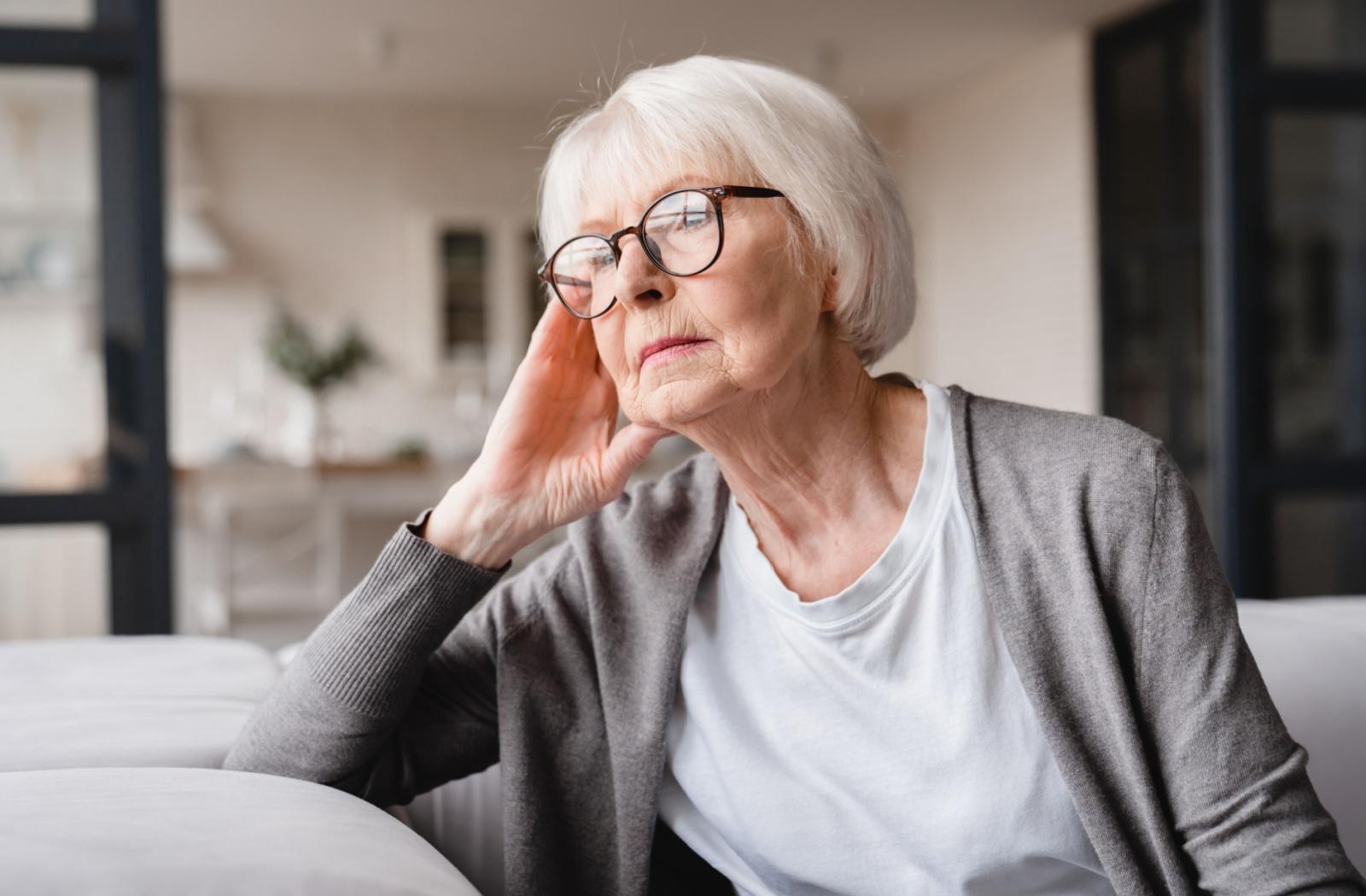 A senior with a wistful expression looks out of a window.