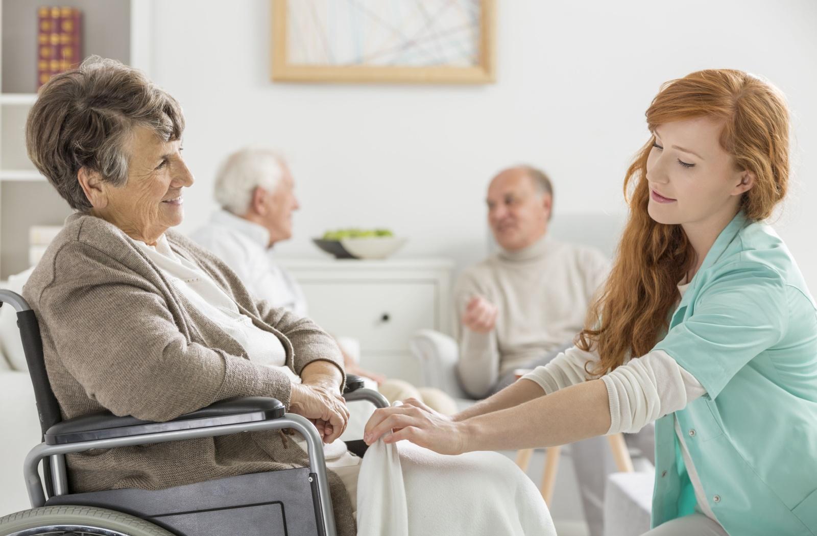 A younger adult places a blanket on their smiling senior grandparent