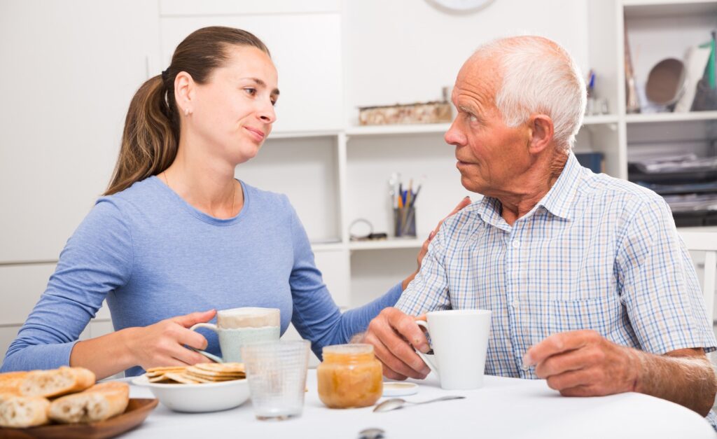 Elderly father and adult daughter having a conversation and drinking tea in the kitchen